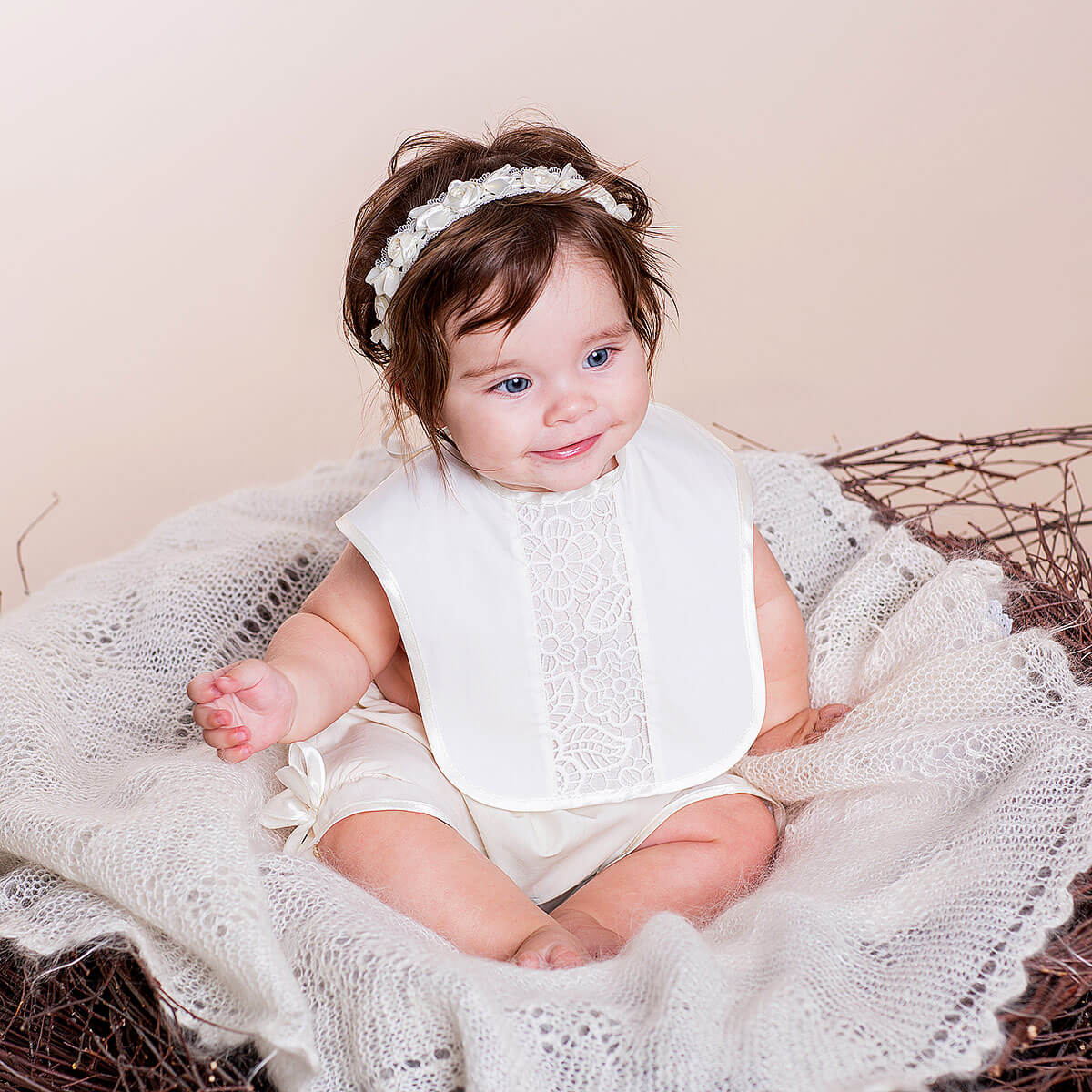 Baby in a Newborn Lace Bib sitting on a textured surface with a neutral background