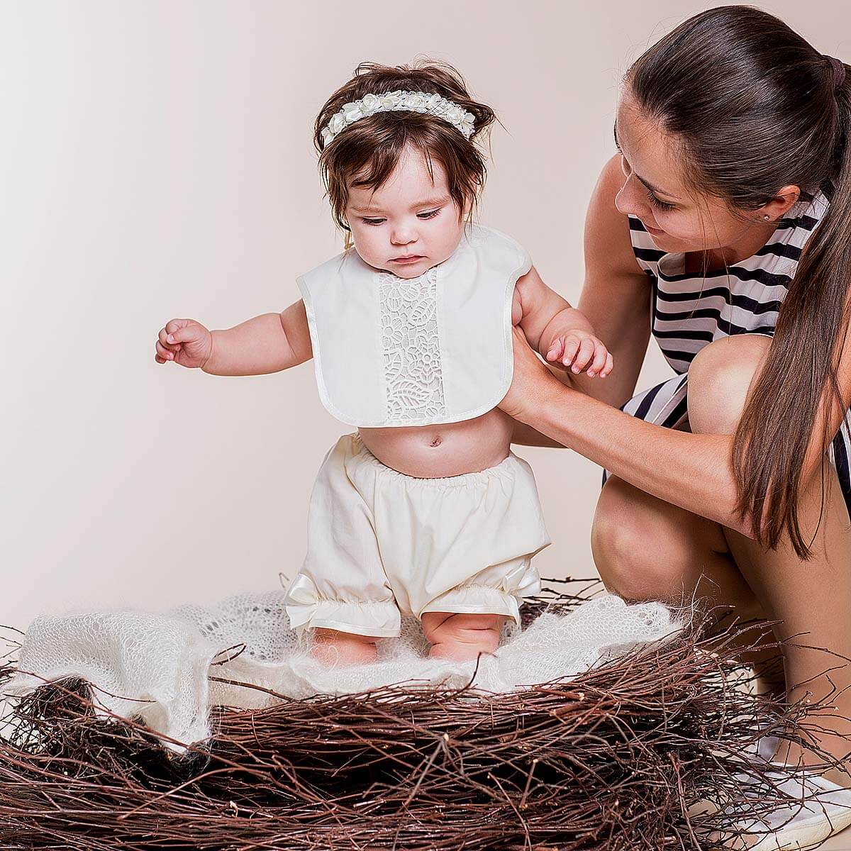 Woman assisting a baby wearing Newborn Lace Bib in a nest-like setting