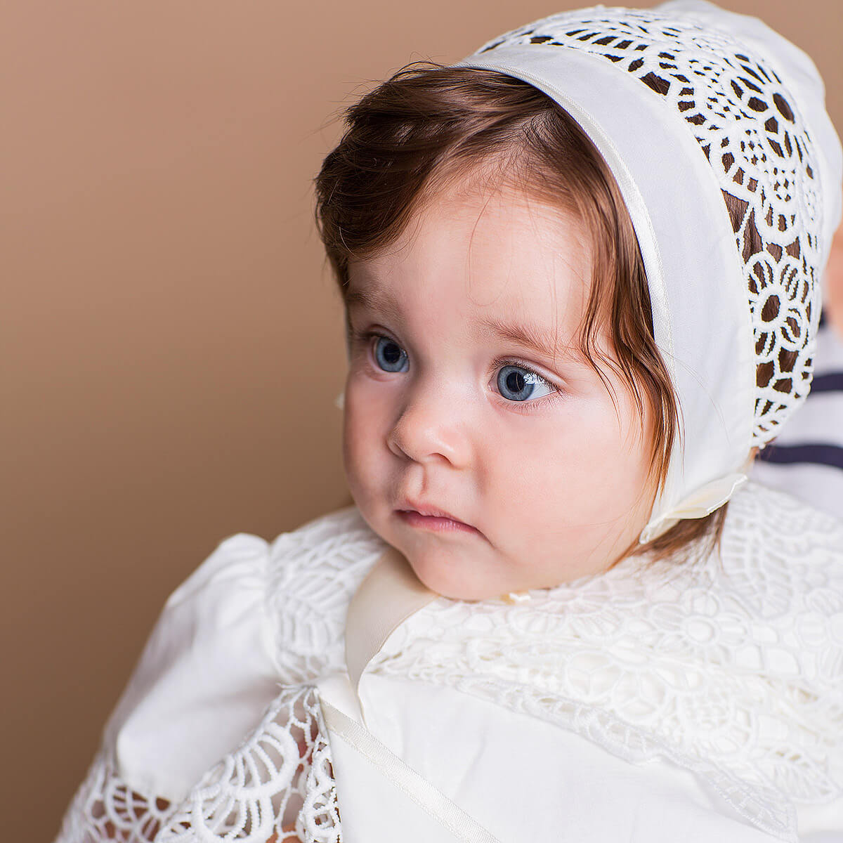 Child wearing a w Lace Baptism Bonnet against a beige background