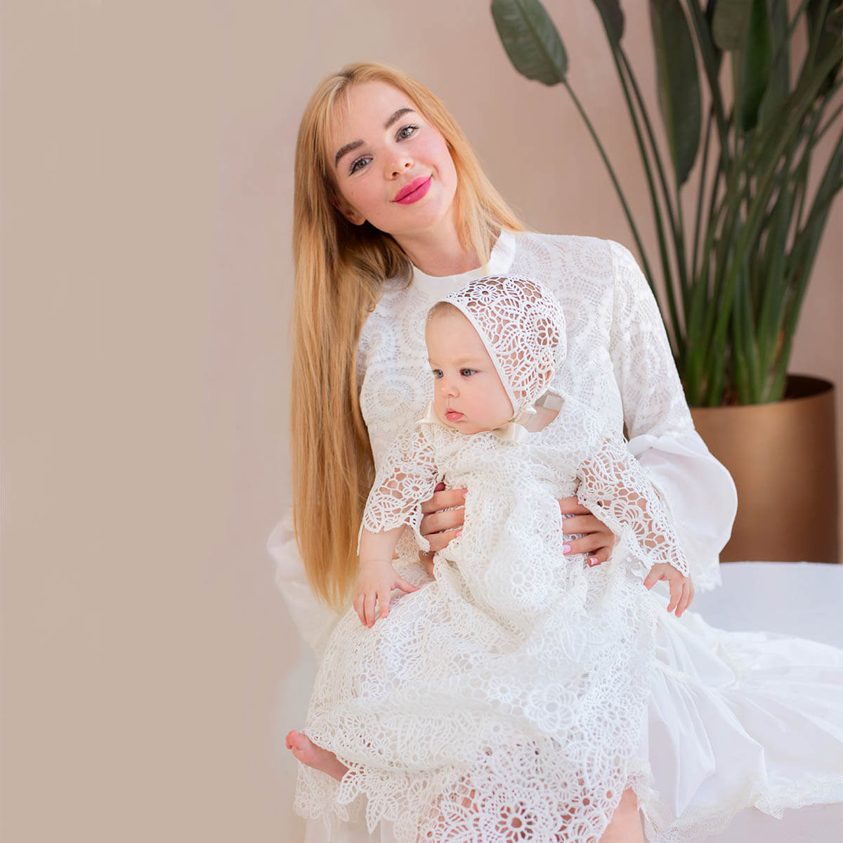 Woman in a white lace dress holding a baby also in a white lace outfit, with a Lace Baptism Bonnet