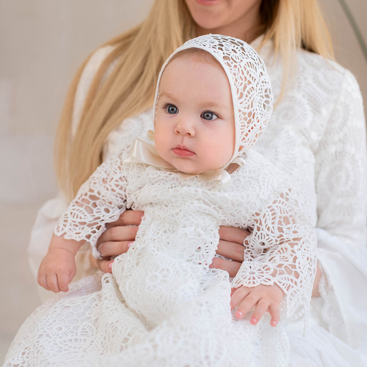 Baby in a Lace Baptism Bonnet held by a person with a neutral background