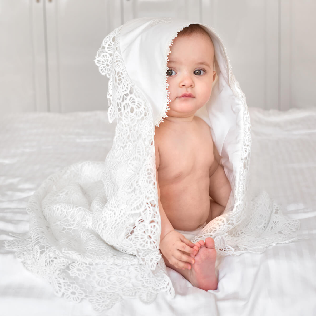 Baby wrapped in a white lace blanket on a soft surface