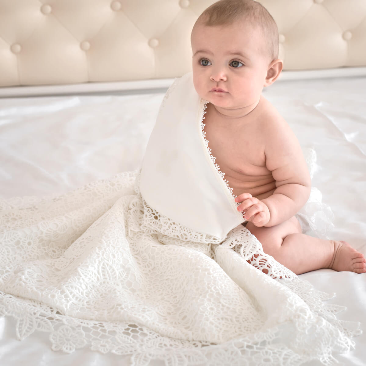 Baby sitting on a bed with a lace blanket
