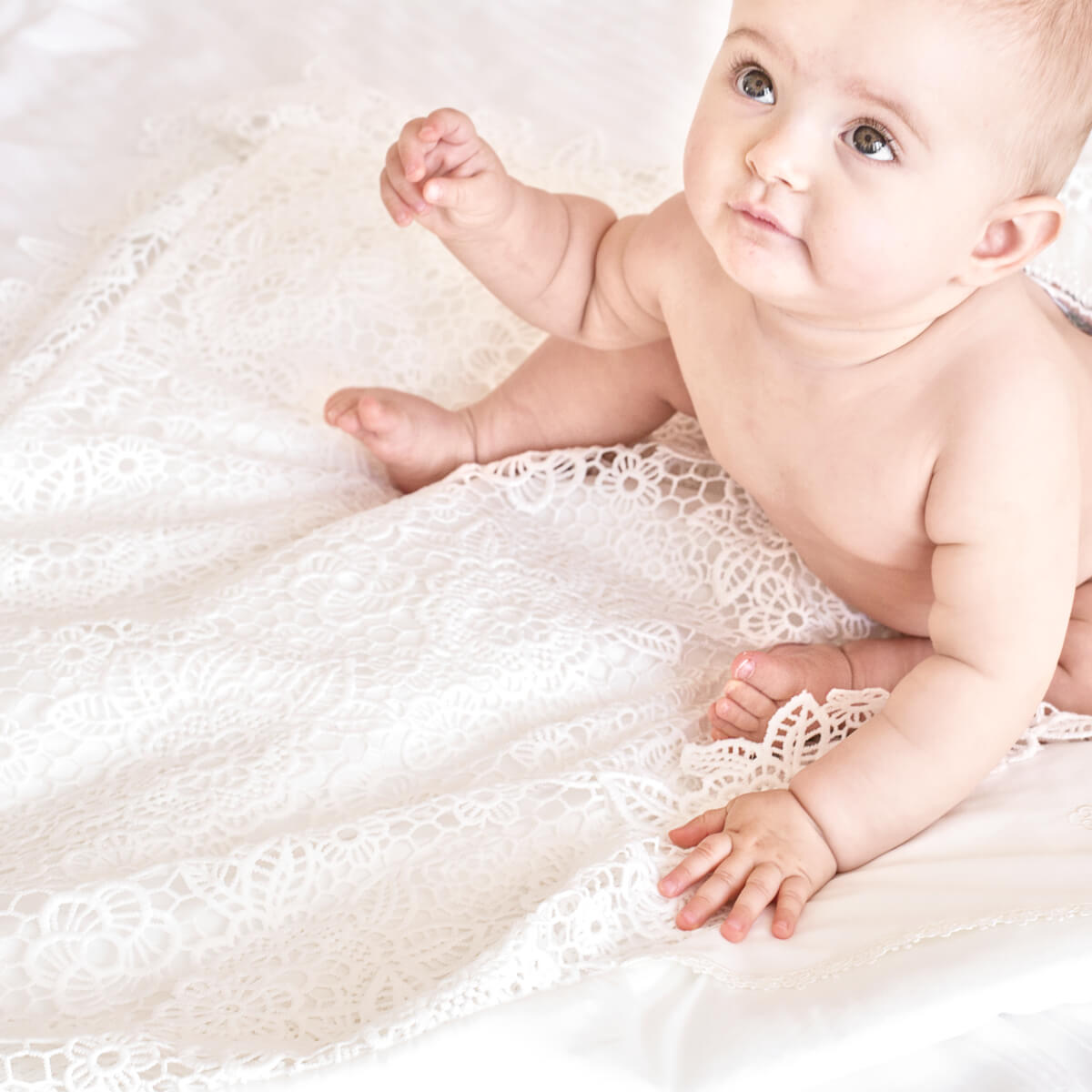 Baby sitting on a white lace baptism blanket