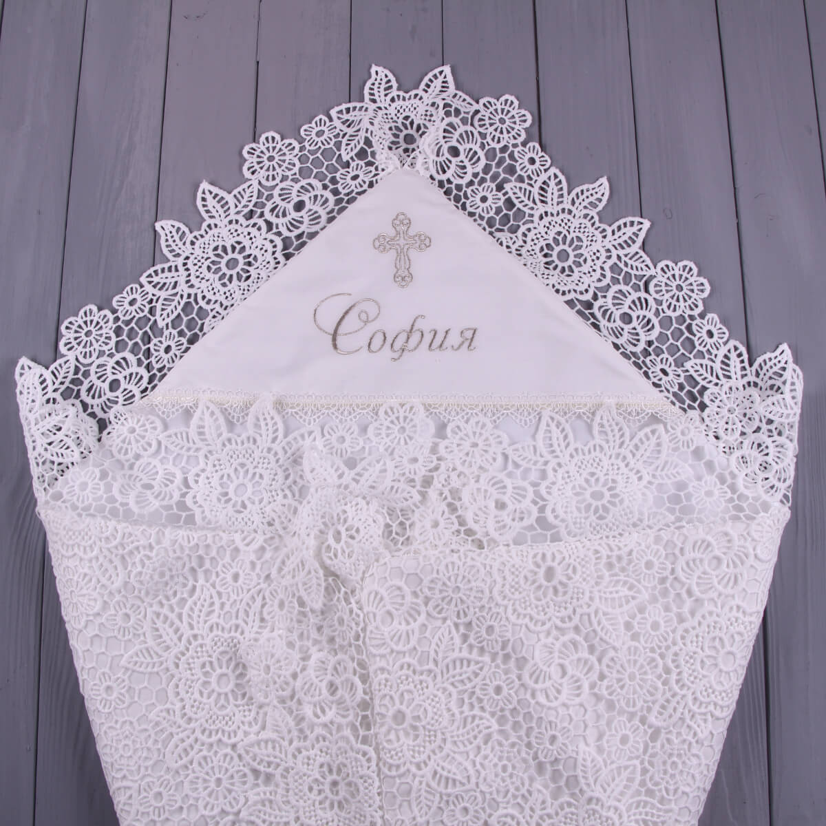 Lace baptism blanket with embroidered name and cross on a wooden background