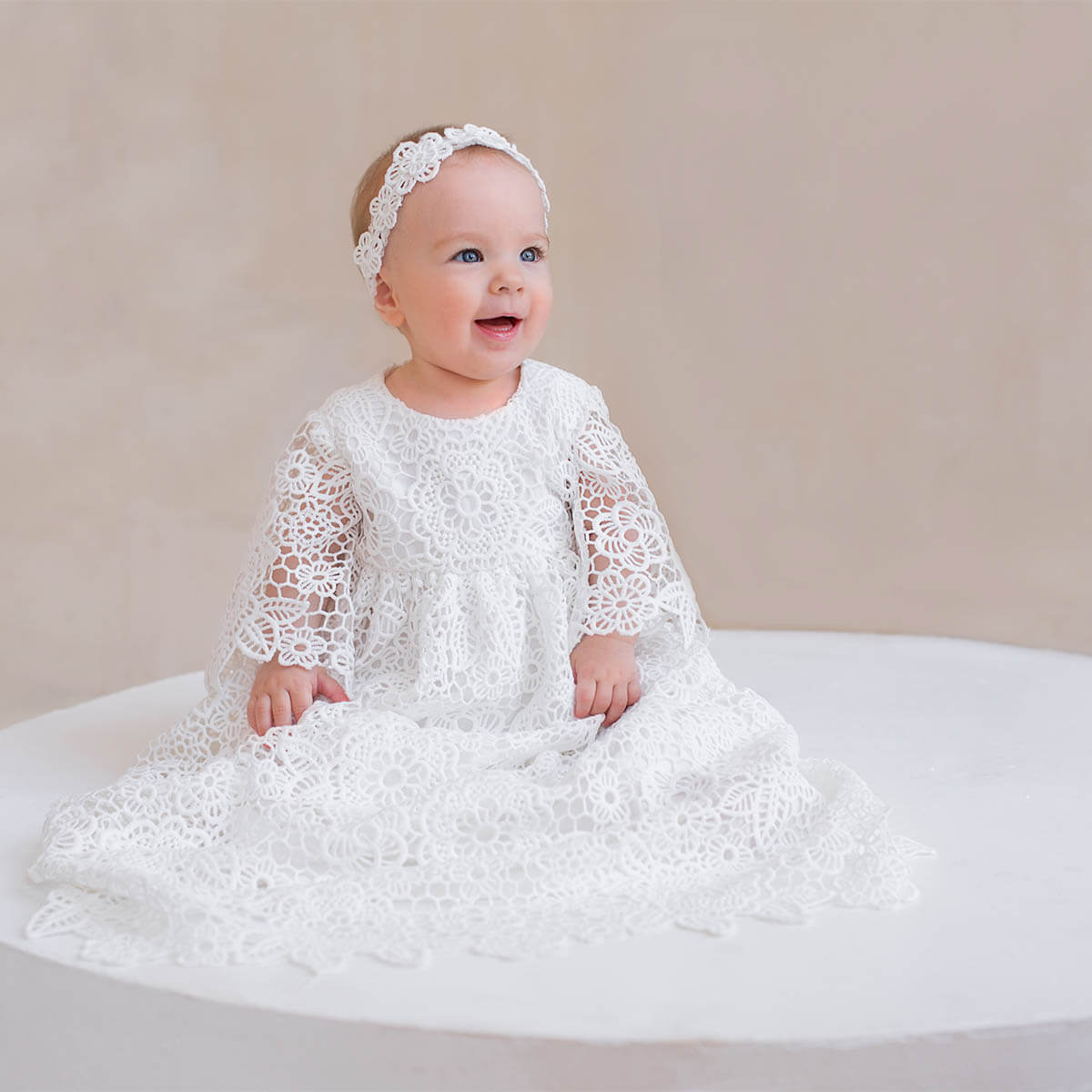 Baby in a Christening Gown for Girls sitting on a white surface with a beige background