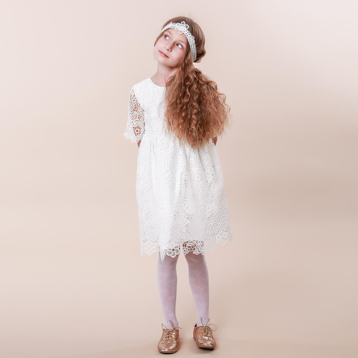 Young girl wearing a white lace dress against a beige background