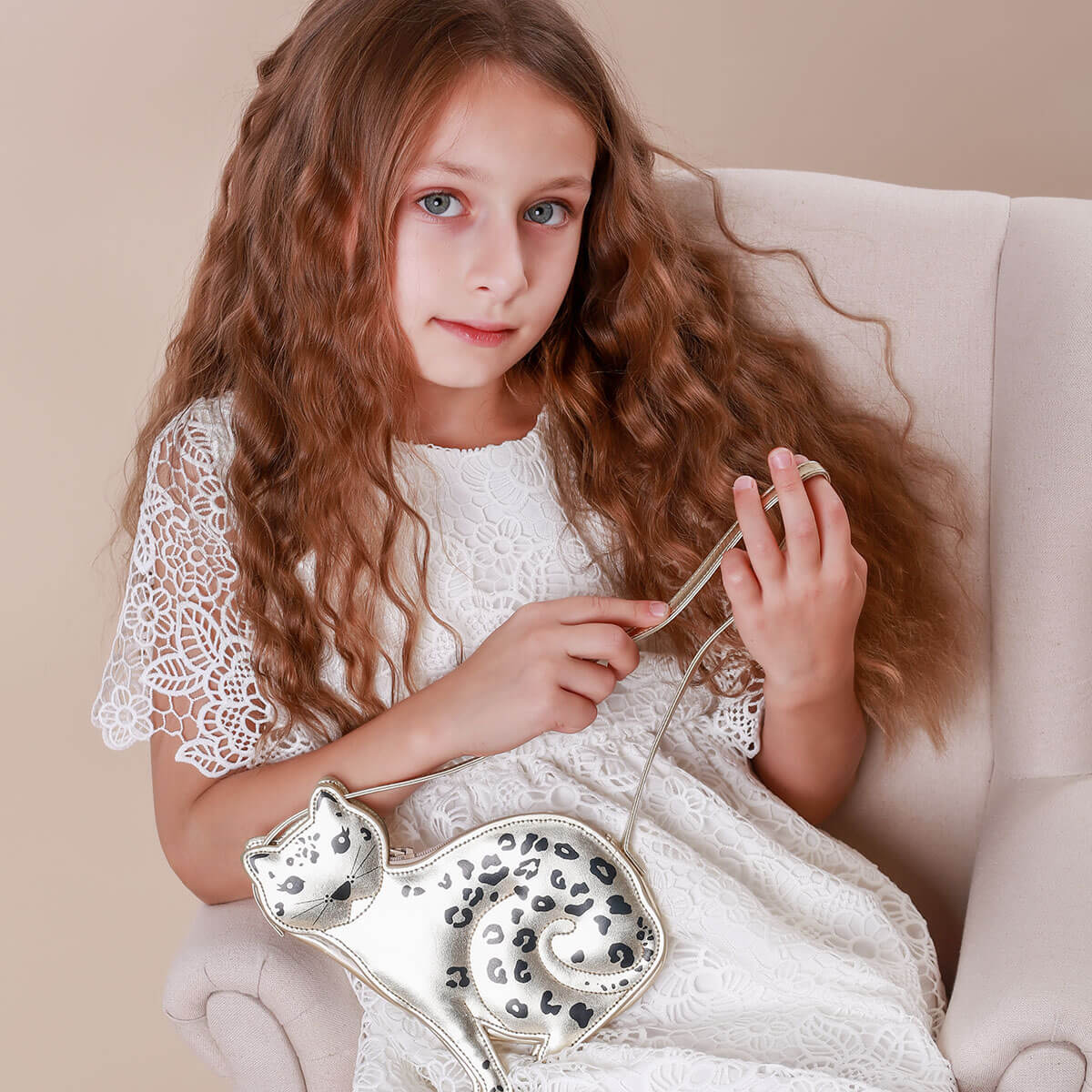 Young girl in a white dress holding a silver handbag with a cat design.