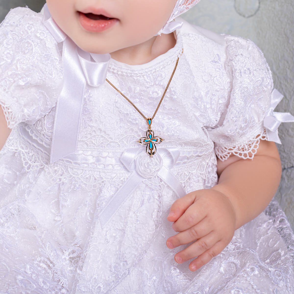 Baby in a white lace dress with a Handmade gold cross pendant