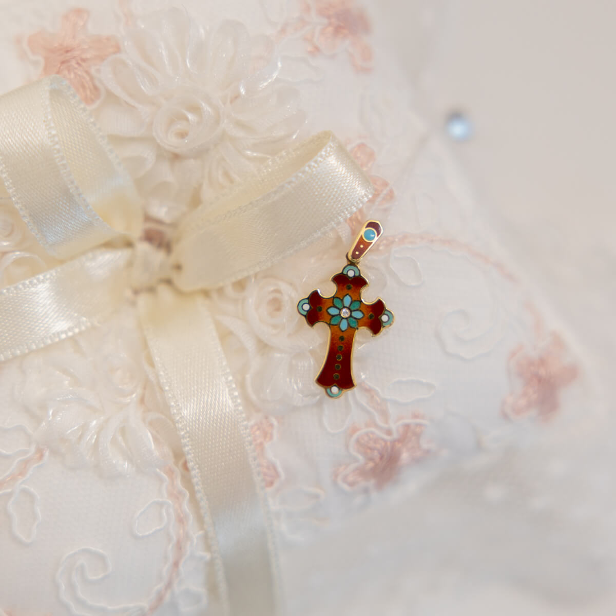 Decorative cross pendant with floral design on a white ribbon against a textured white background