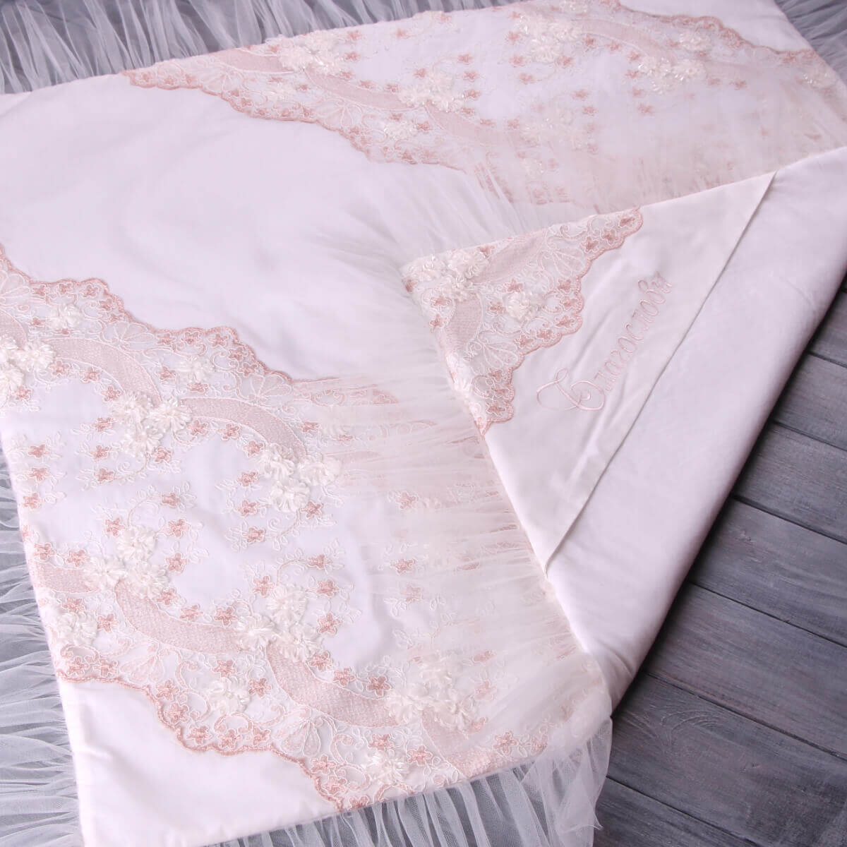 White baptism blanket with pink lace detailing on a wooden surface