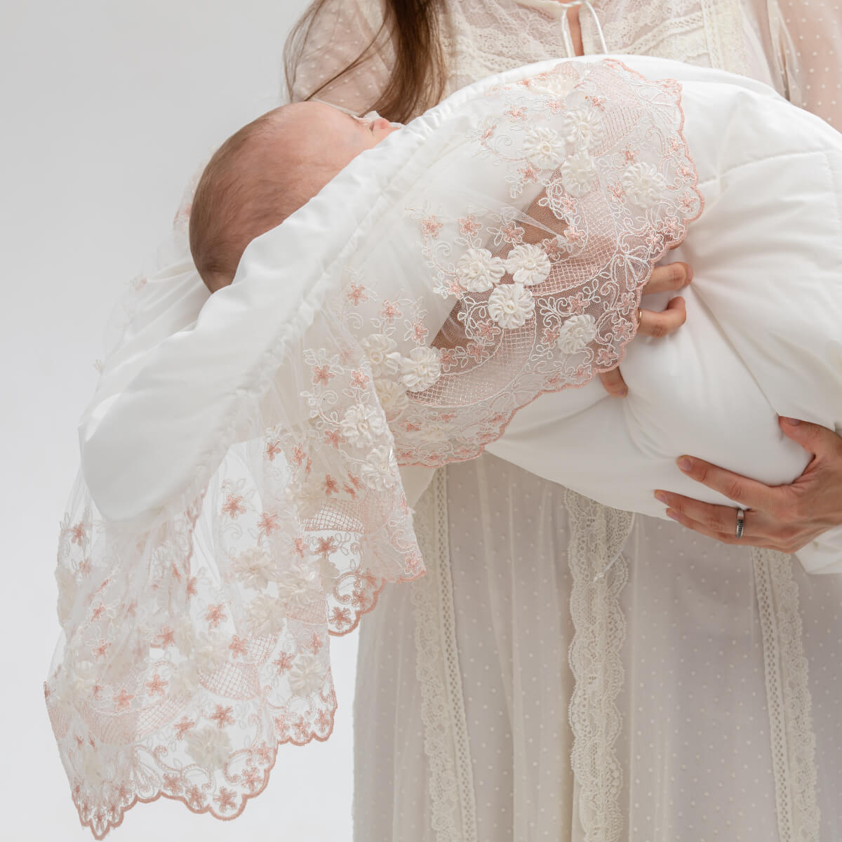 Woman holding a baby wrapped in a Coming Home Blanket  against a plain background