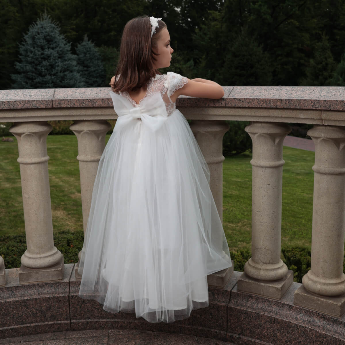 Young girl in a white dress standing on a stone staircase with greenery in the background