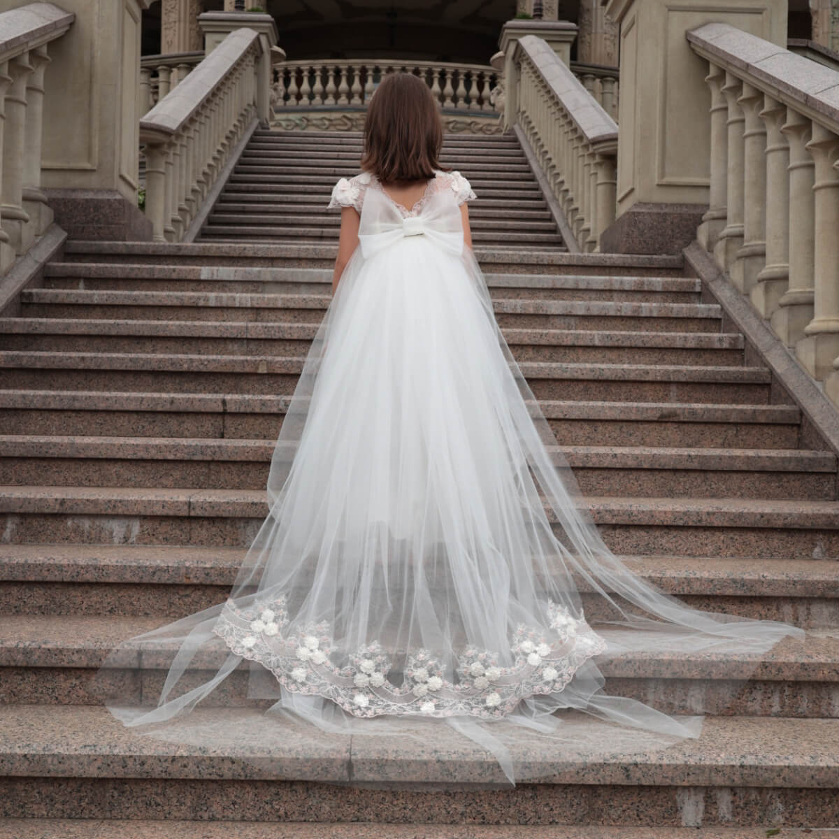 Woman in a flower girl dress with detachable train standing on stone steps 