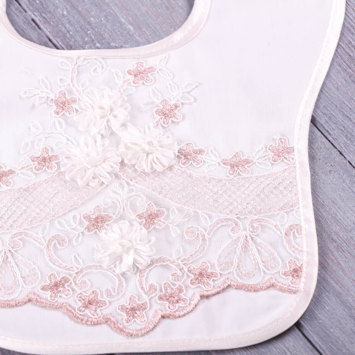 Baptism Bib with Lace  with pink floral lace embroidery on a wooden surface