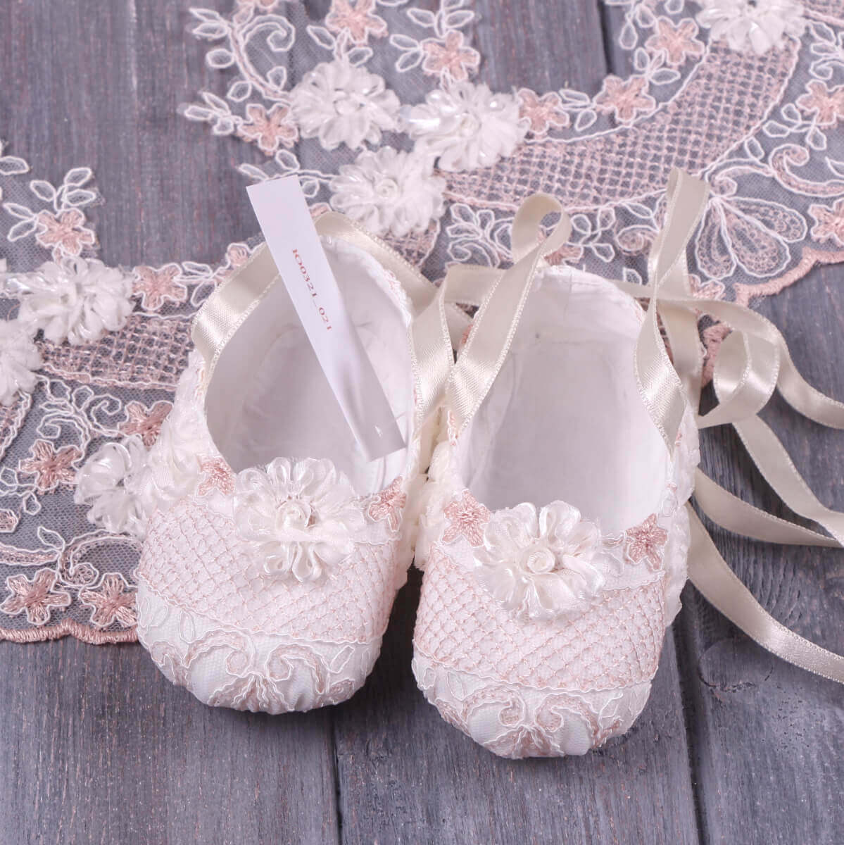 Pair of  Christening Booties on a wooden surface with decorative ribbons and flowers.
