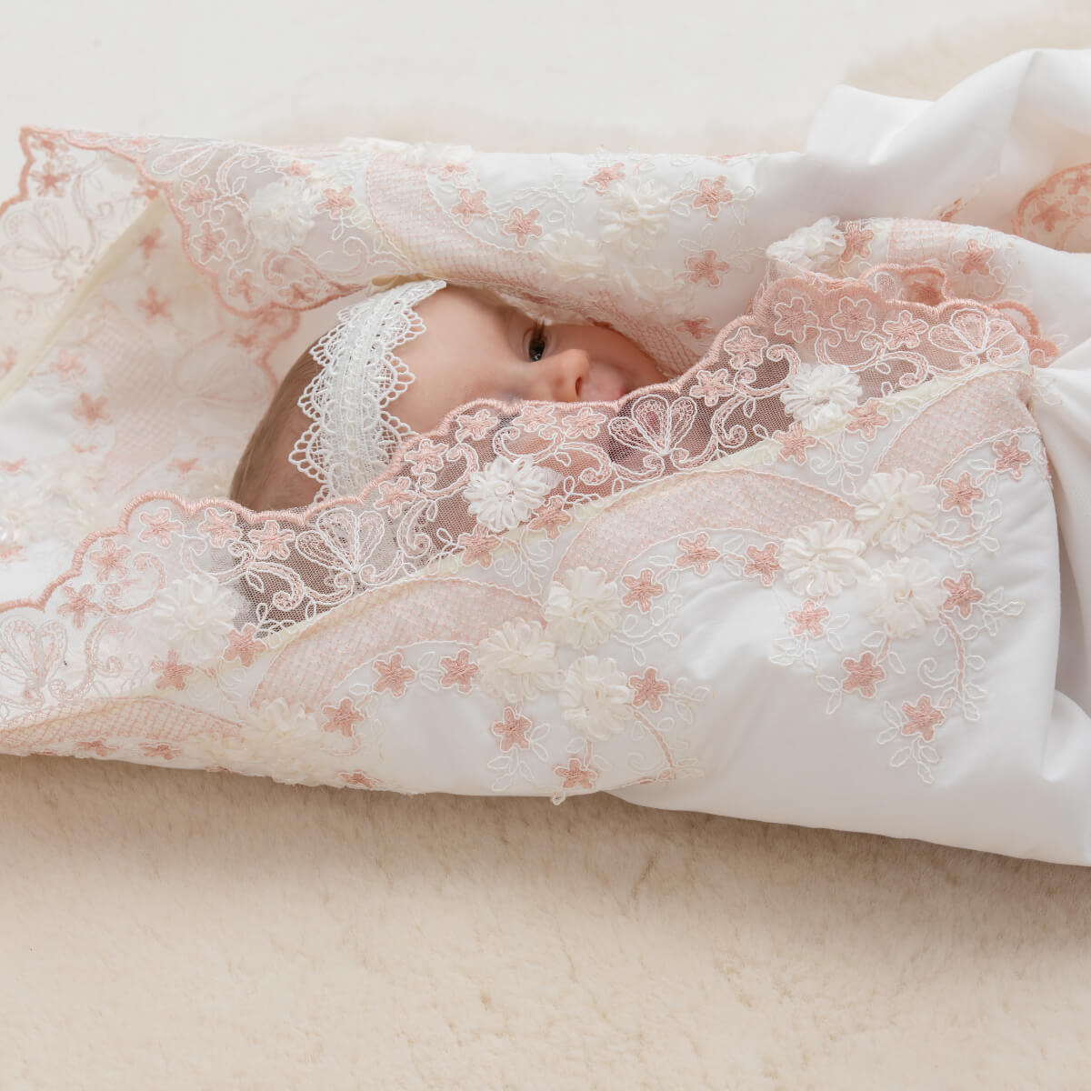Baby wrapped in a lace blanket on a soft surface