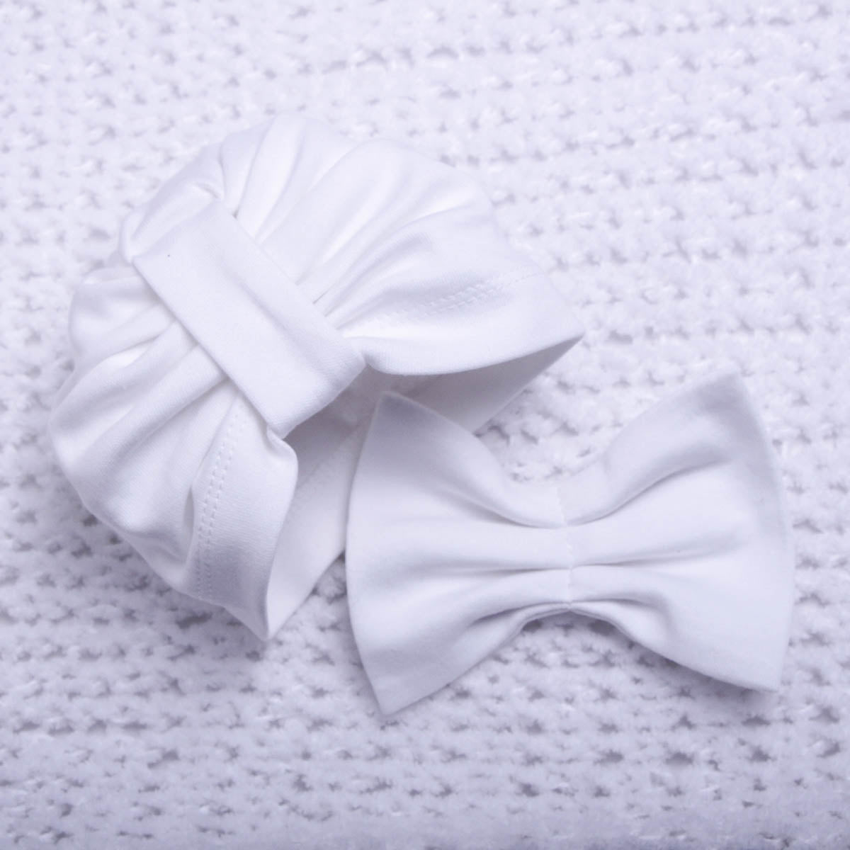White baby beanie with a bow on a textured gray background