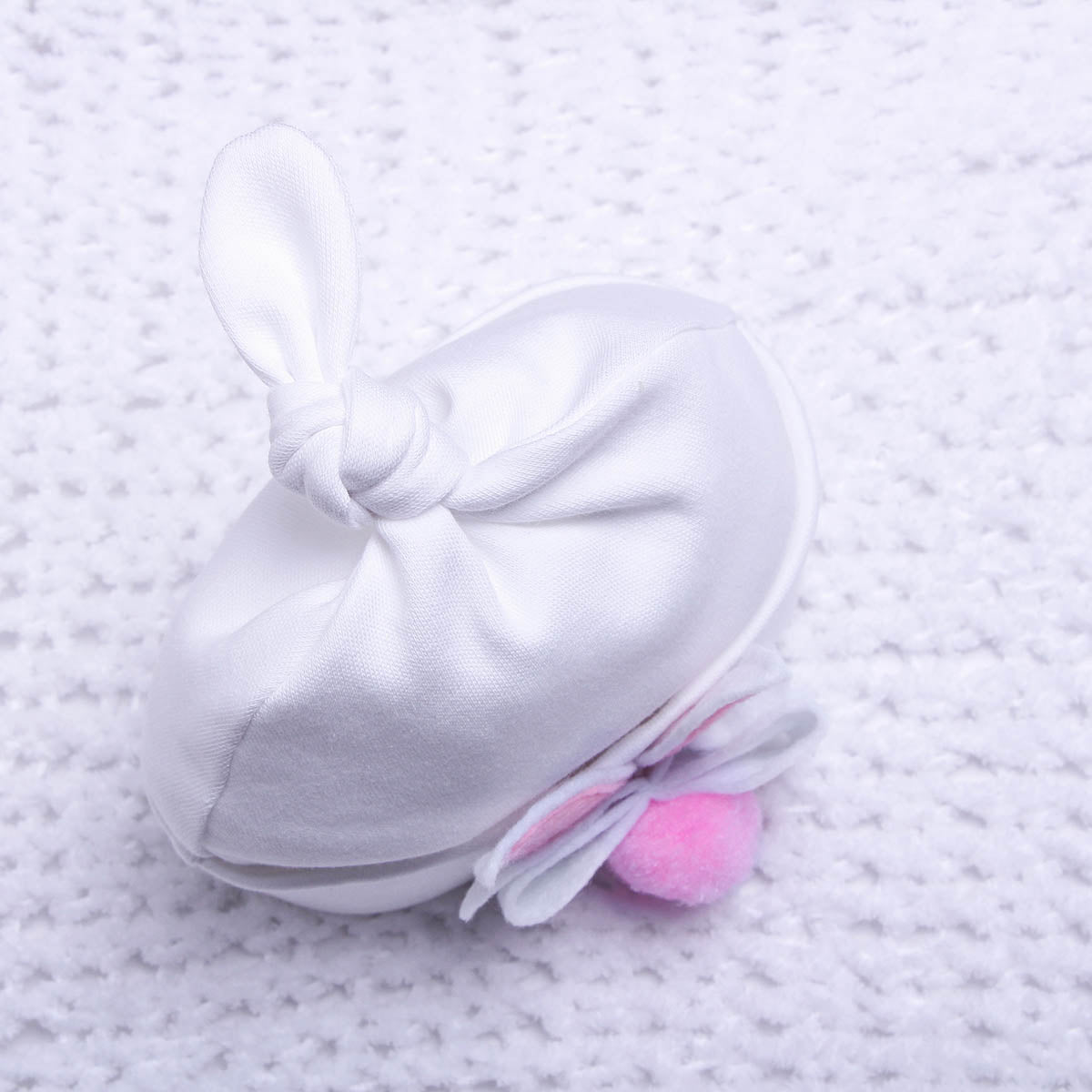 White baby hat with a pink pom-pom on a textured white background