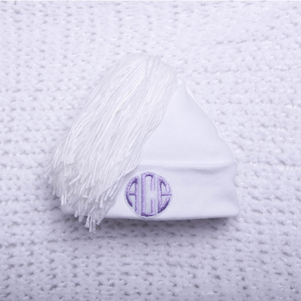 White beanie with purple monogram on a textured gray background