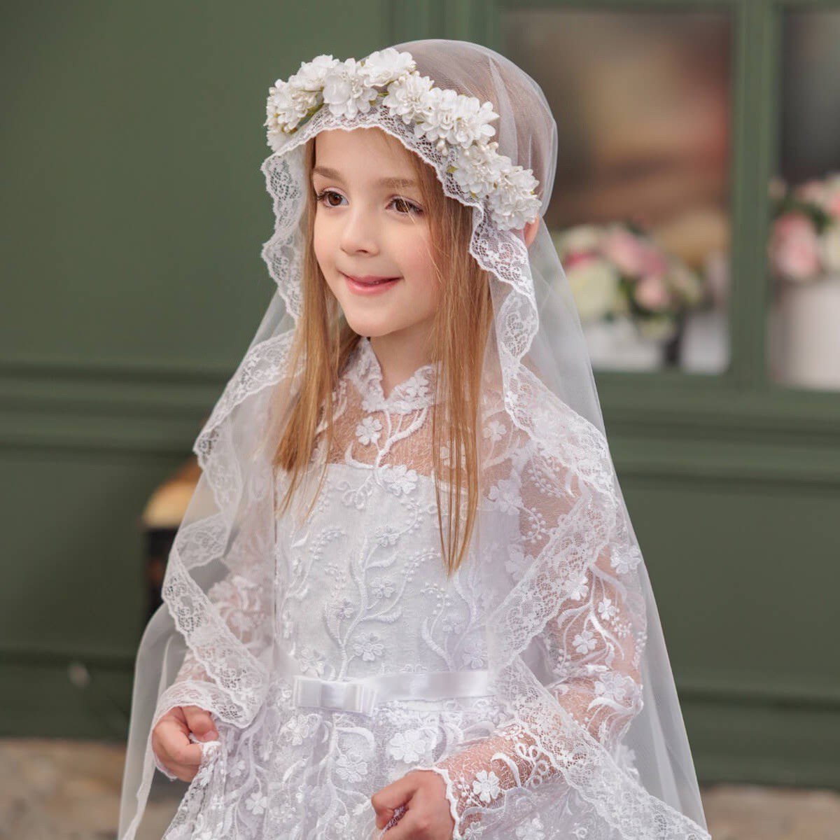 Young girl in Communion Dress with Flower Wreath Veil against a blurred background.