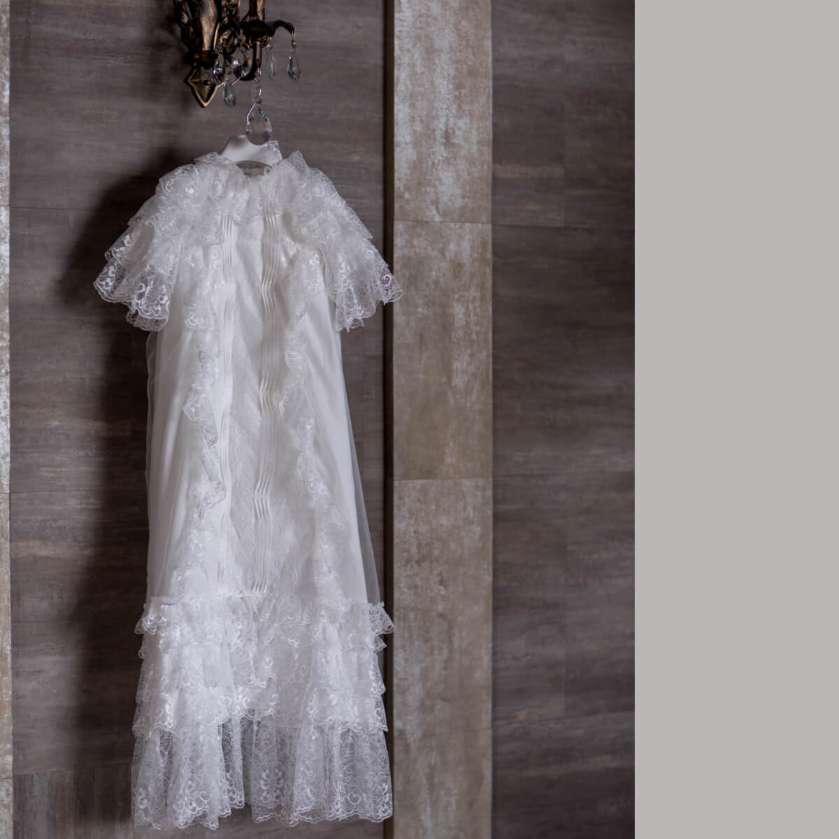 White lace christening dress hanging on a wooden wall