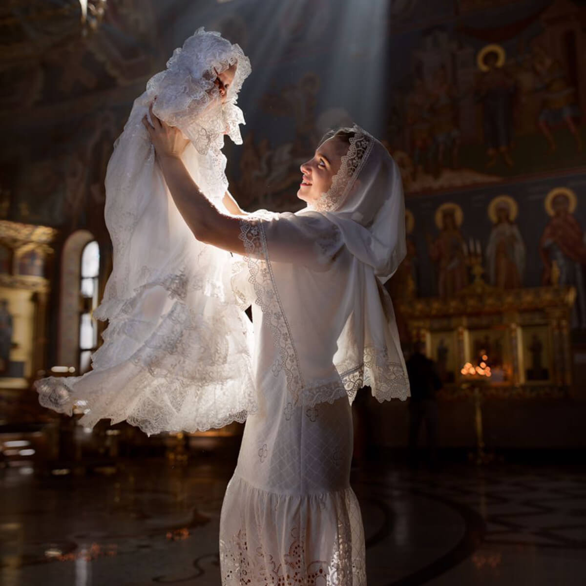 Woman in a white dress holding a baby in a christening gown