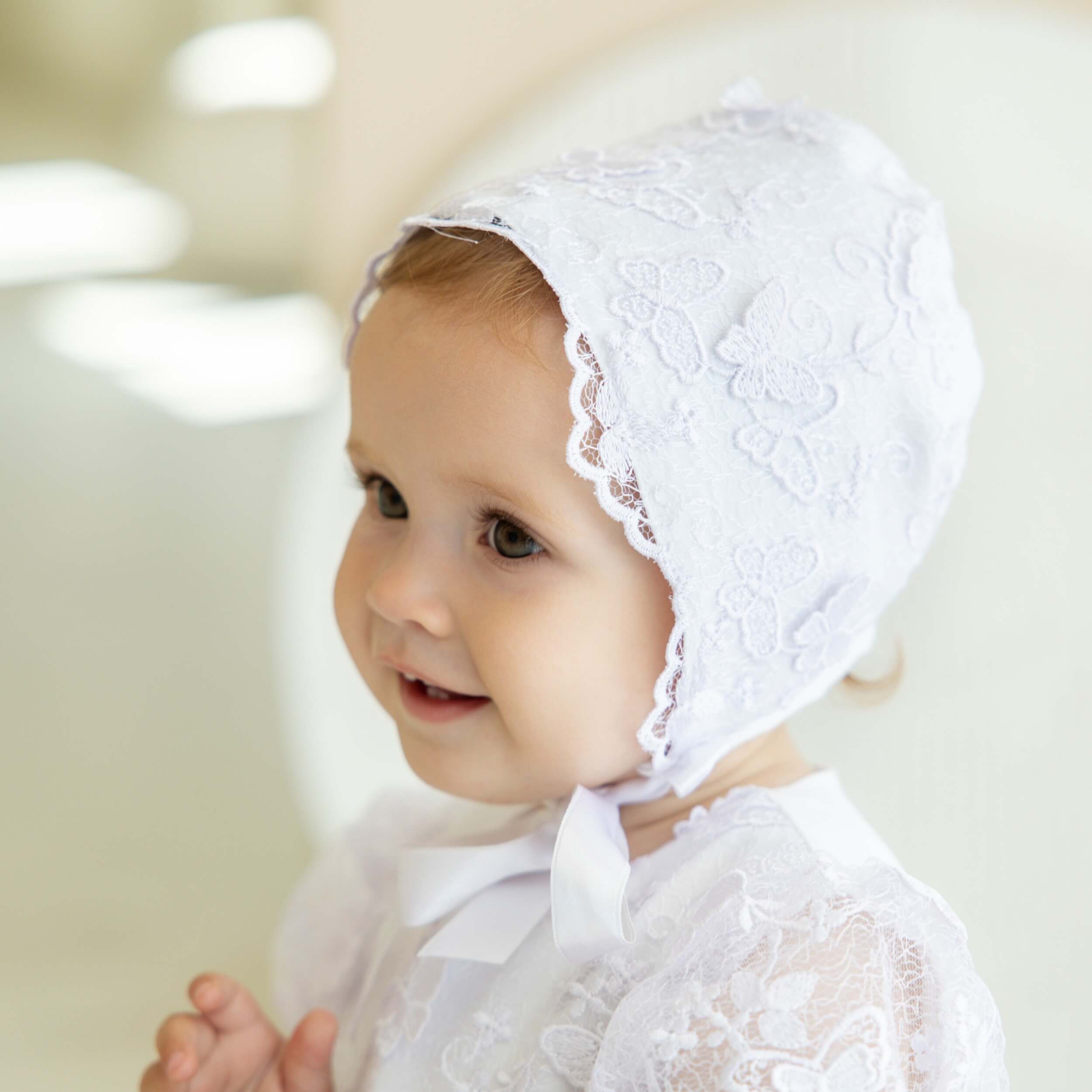 Baby wearing a lace baptism bonnet t against a blurred background