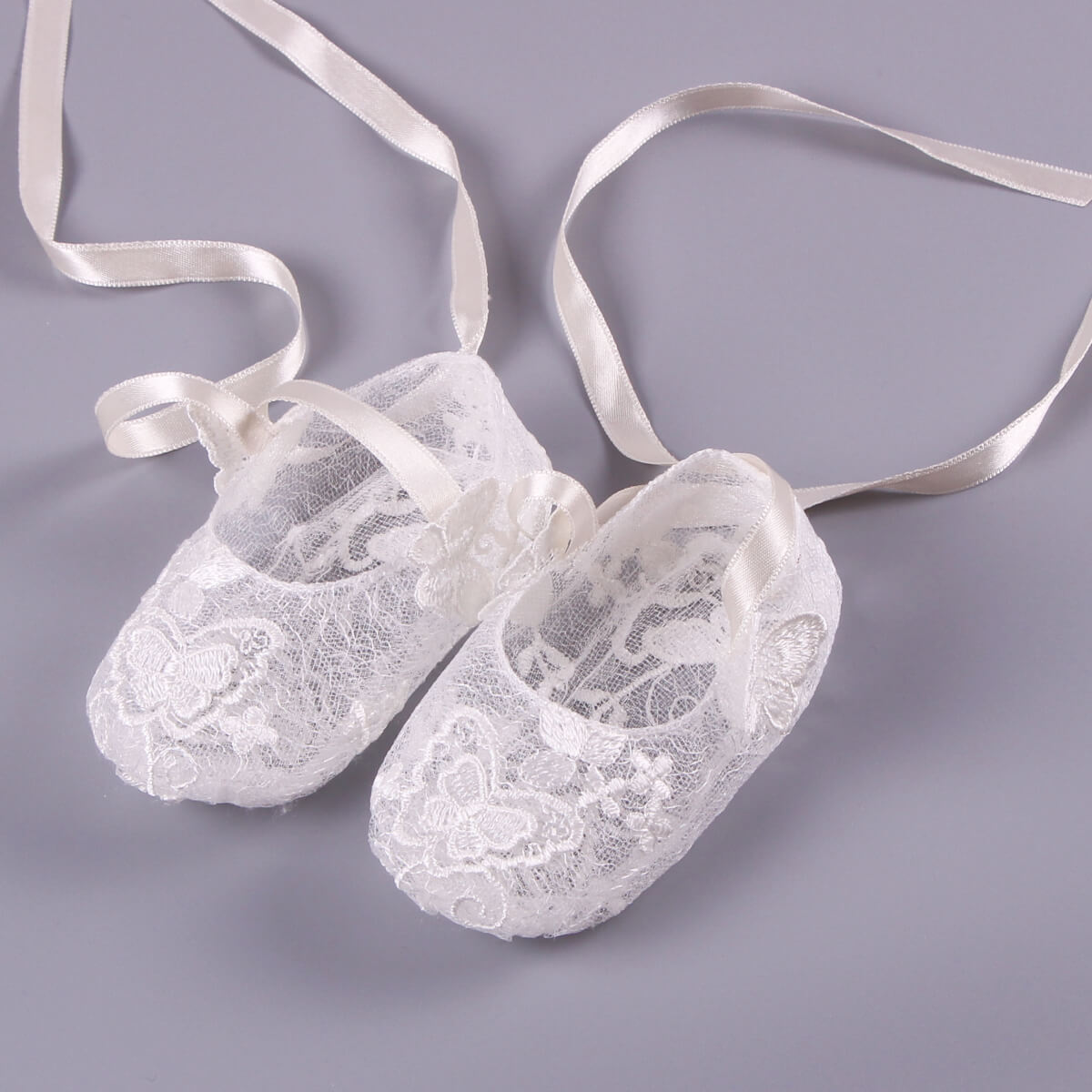Pair of  Christening Lace Booties  with ribbons on a gray background