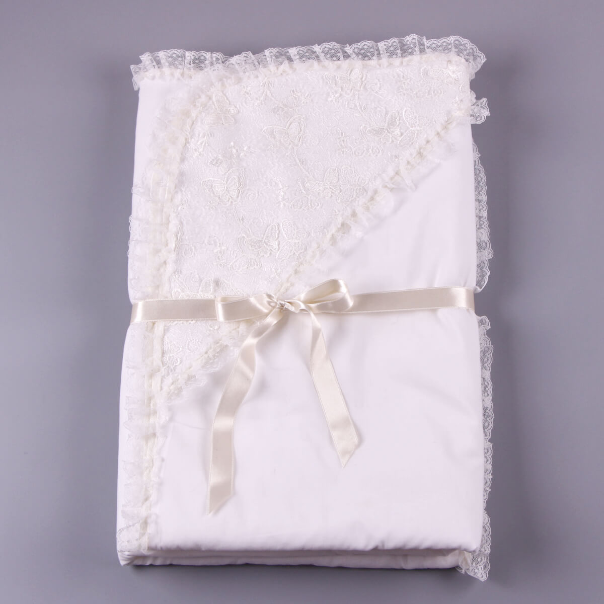 Folded white lace christening blanket with a ribbon on a gray background