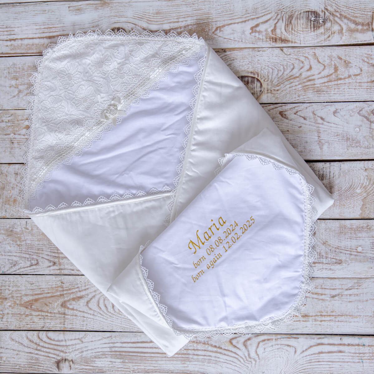 Set of embroidered ivory baptism blanket on a wooden surface