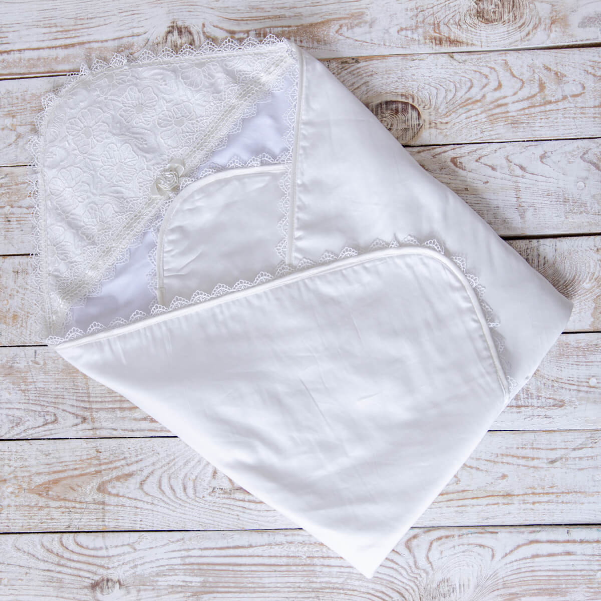 Set of ivory baptism blanket with lace trim on a wooden surface