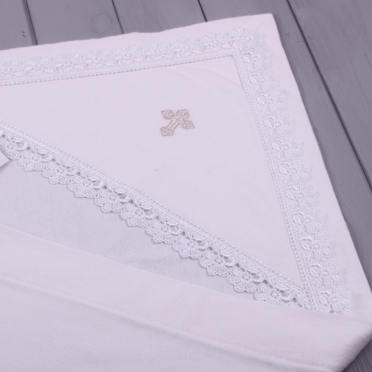 White embroidered baptism blanket with lace trim on a wooden surface