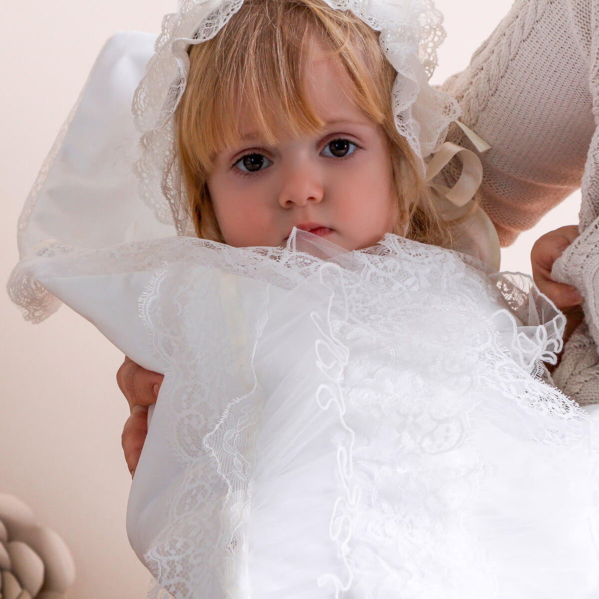 Child wearing a white christening blanket held by an adult.