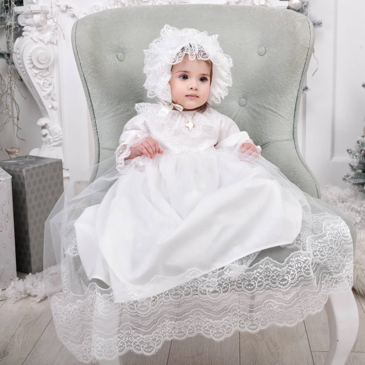 Baby in a Christening Gown for Girls sitting on a gray chair