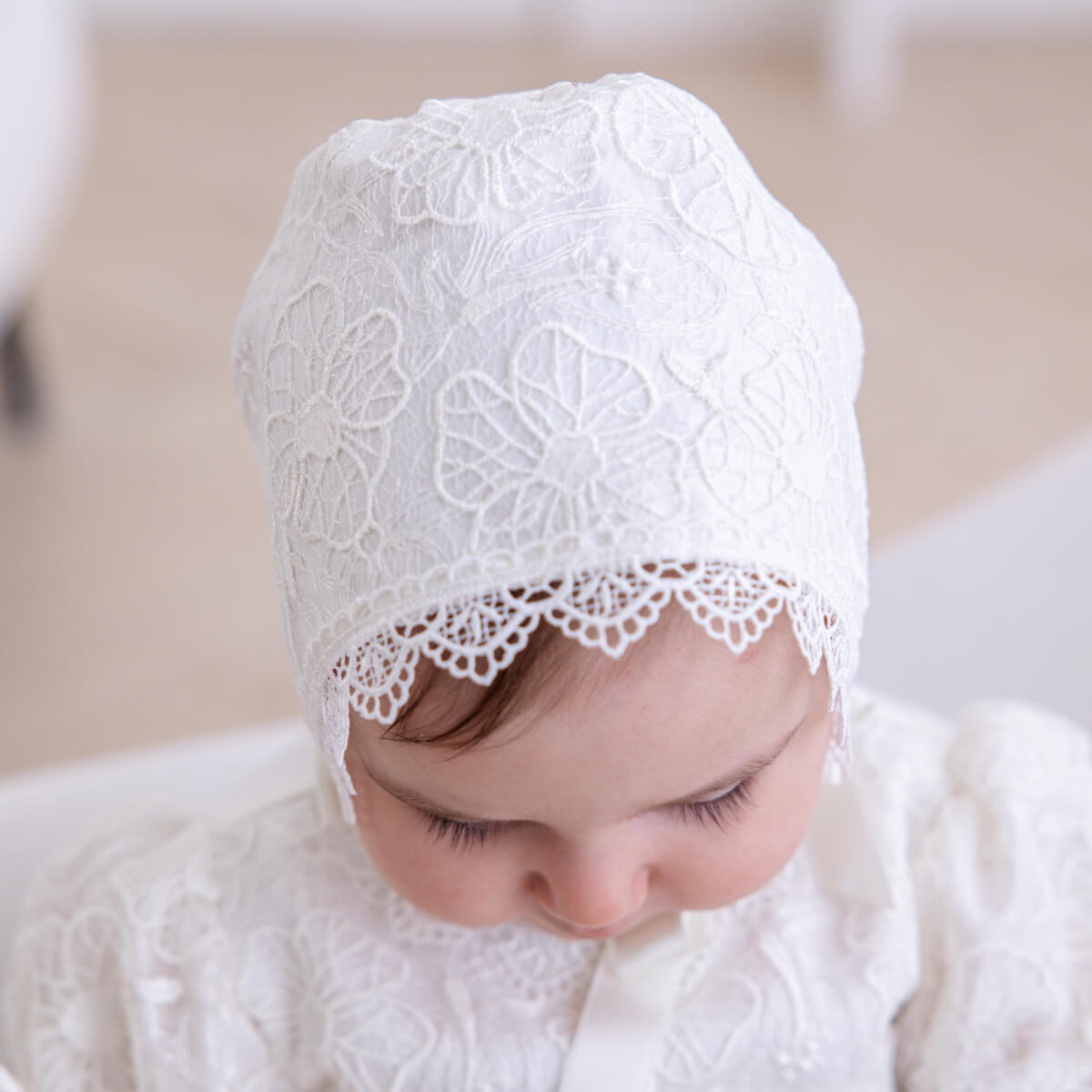 Baby wearing a Cotton Baptism Bonnet against a neutral background