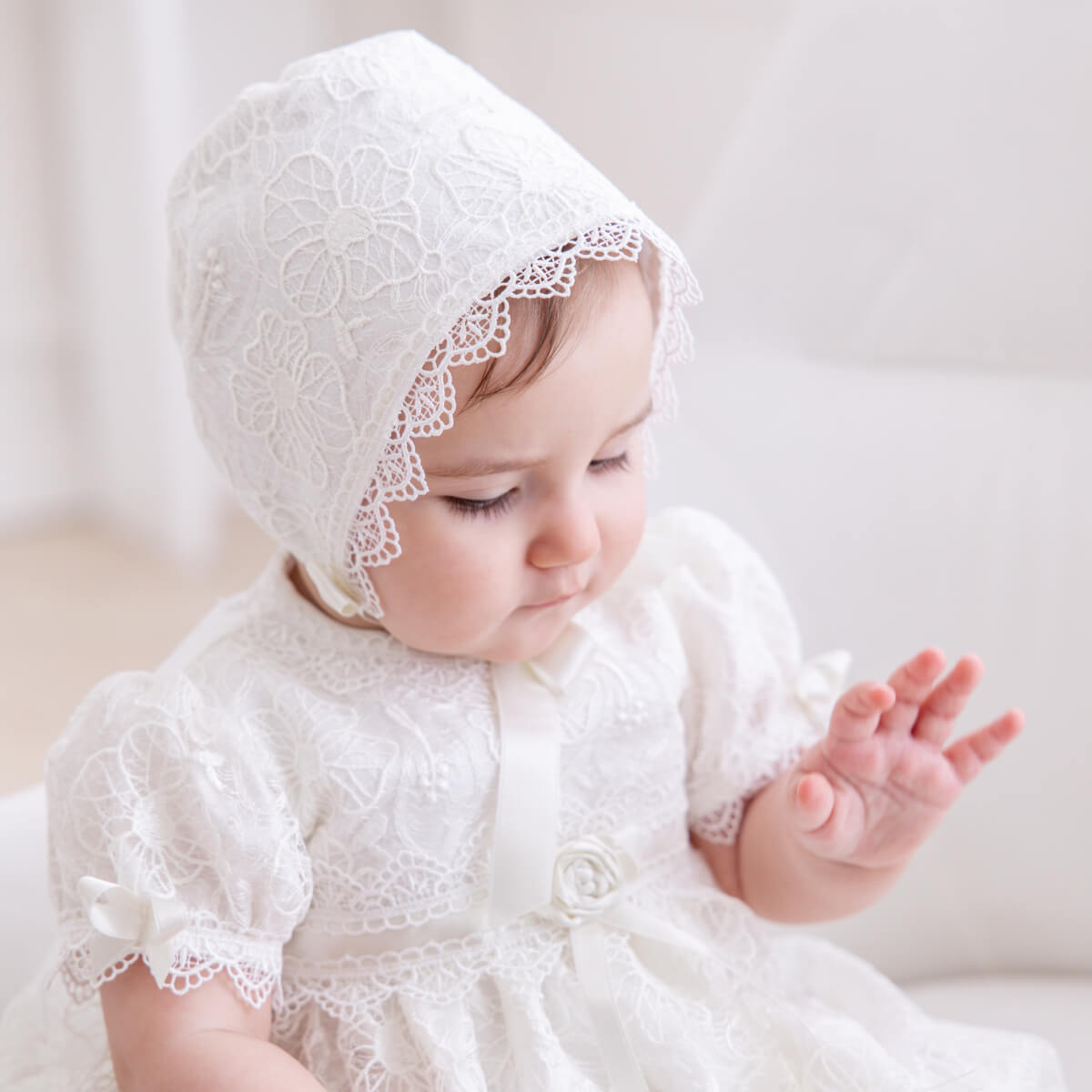 Baby wearing a Cotton Baptism Bonnet and dress against a plain background