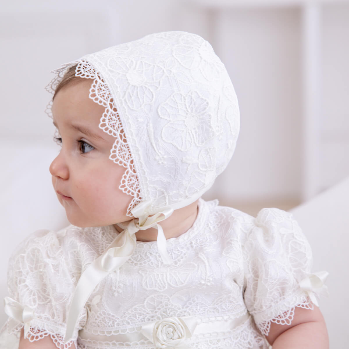 Baby wearing a Cotton Baptism Bonnet against a neutral background