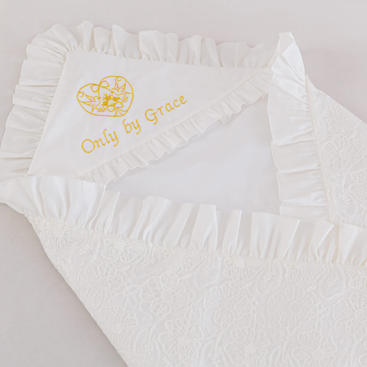 White baby outfit with ruffled details and 'Only by Grace' embroidery on a light background