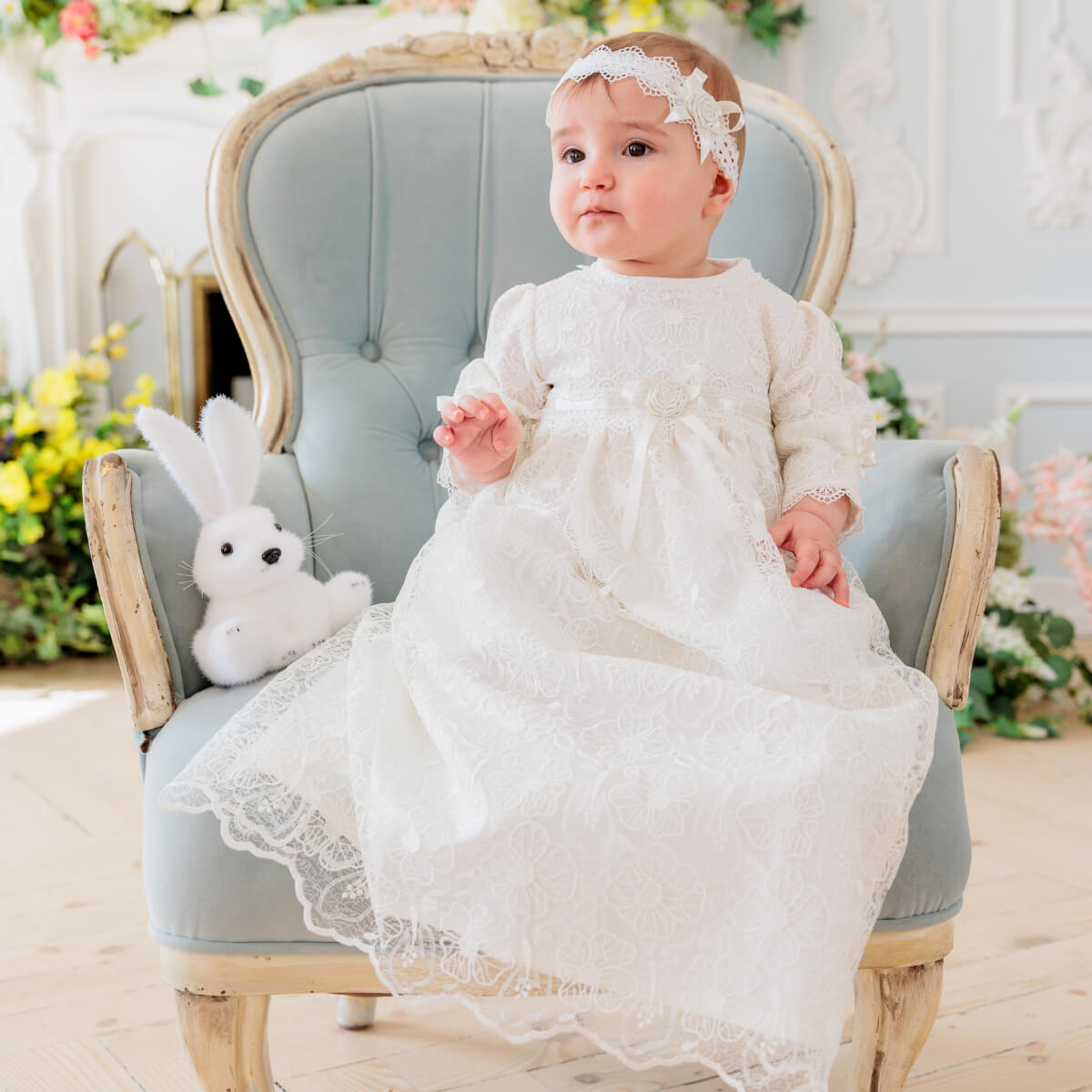 Baby in a Christening Gown for Girls sitting on a light blue chair 