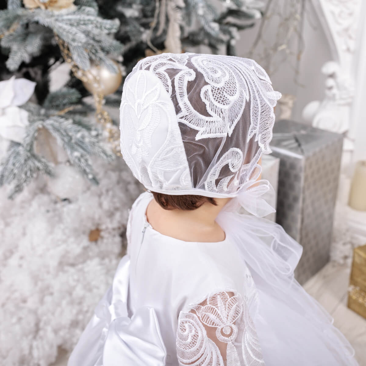 Person wearing a white lace bonnet in a festive setting with White Baptism Dress and decorations.