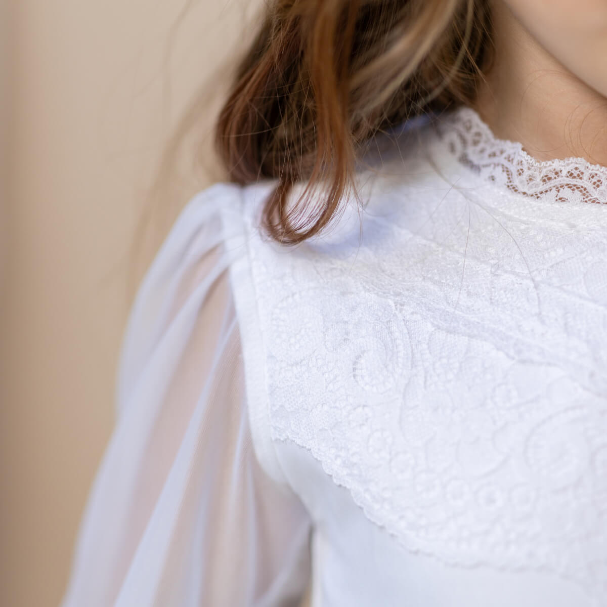 Close-up of a person wearing a white lace top with sheer sleeves against a beige background
