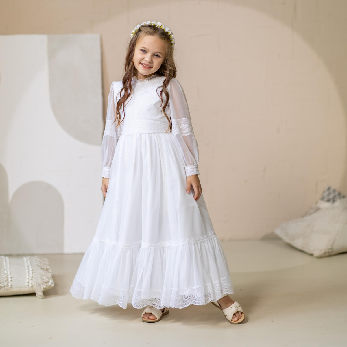 Young girl in a Lace Communion Dress standing against a beige wall.