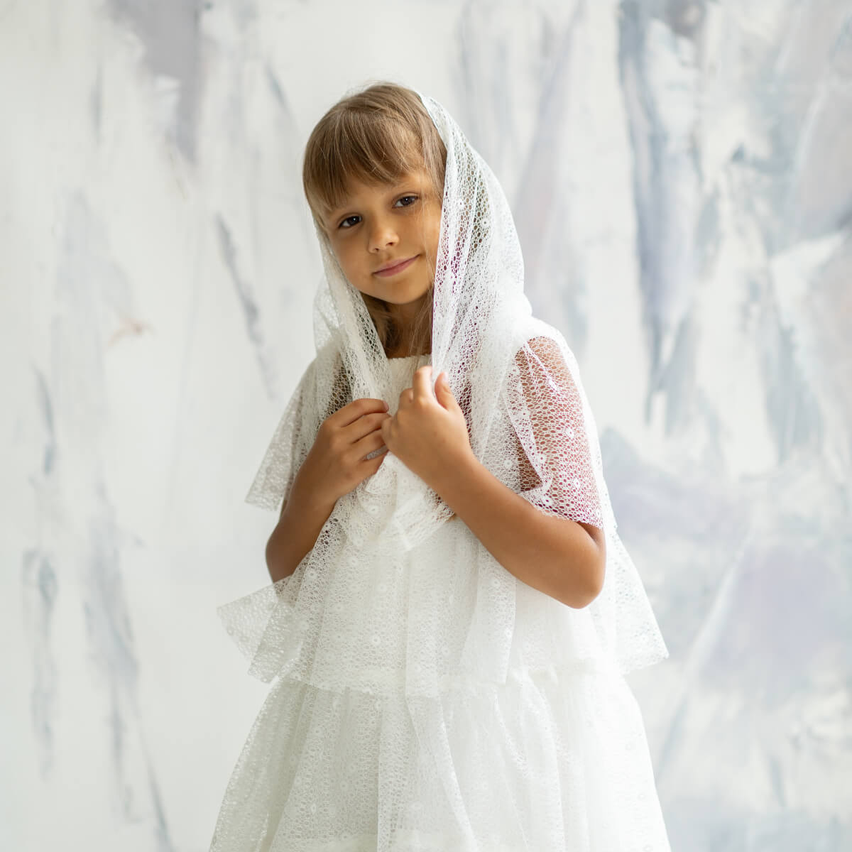 Young girl wearing a First Communion Mantilla Veil against a light background