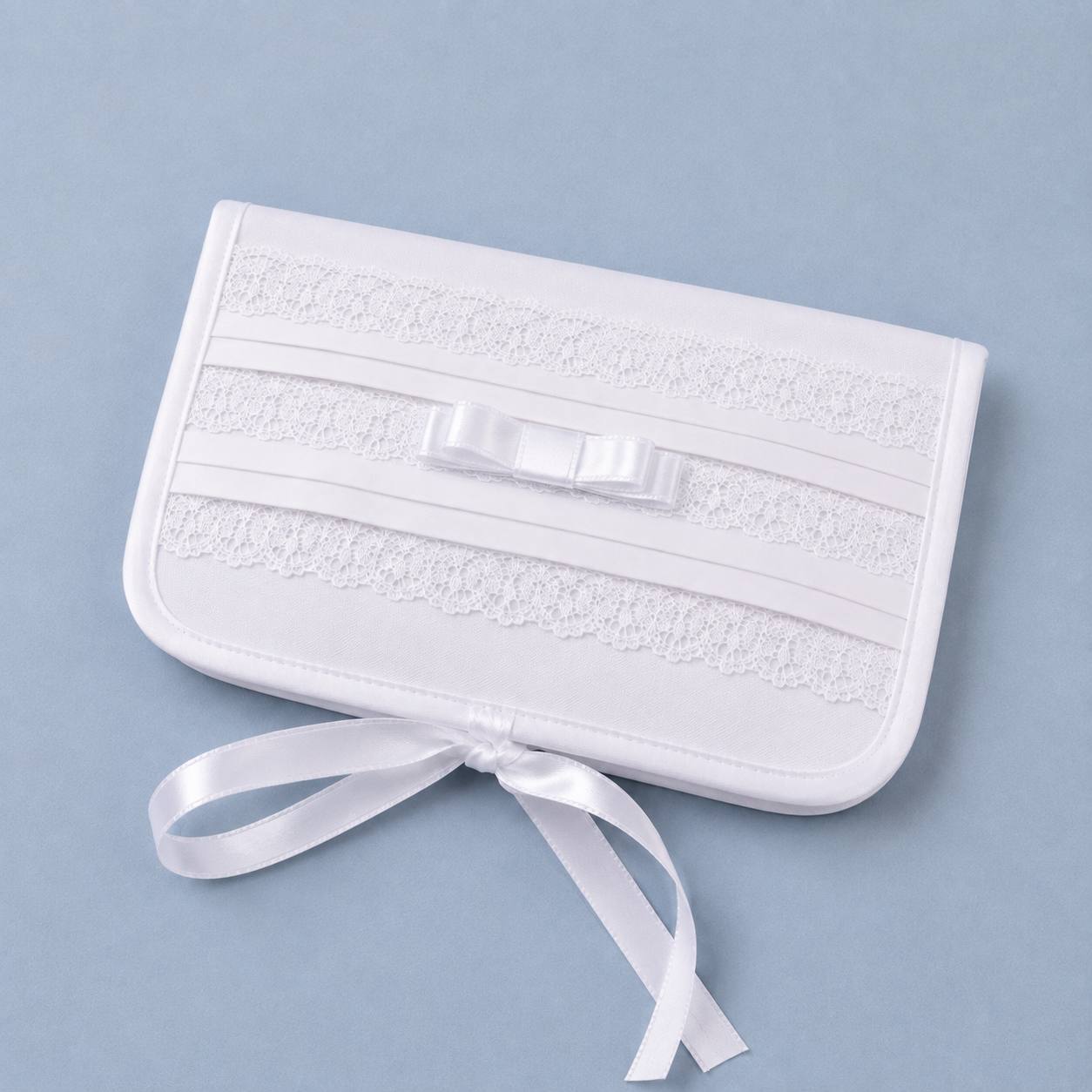 A white satin and lace first curl keepsake box with a matching satin ribbon bow on top and a long ribbon tail, photographed on a solid light blue background.