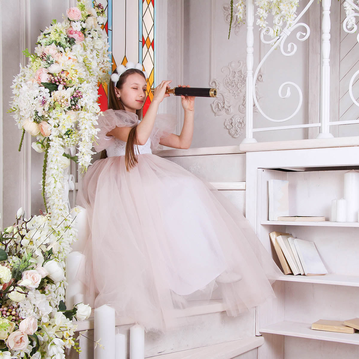 Young girl in a white dress sitting on a staircase surrounded by floral decorations.