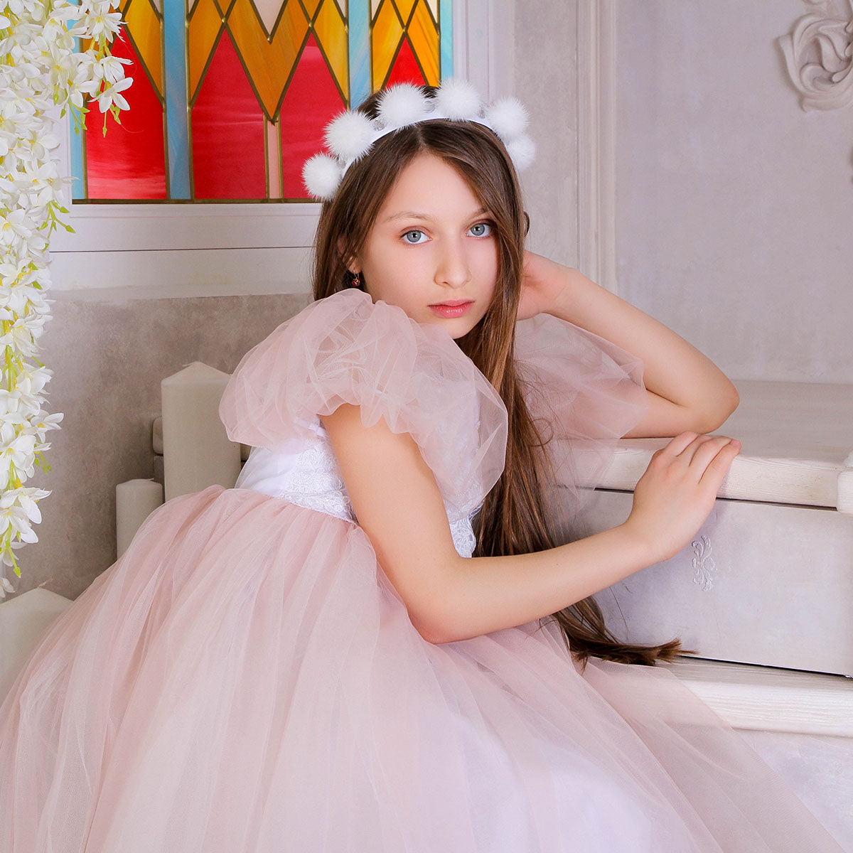 Young girl in a pink dress with a decorative headband sitting in a decorated room.