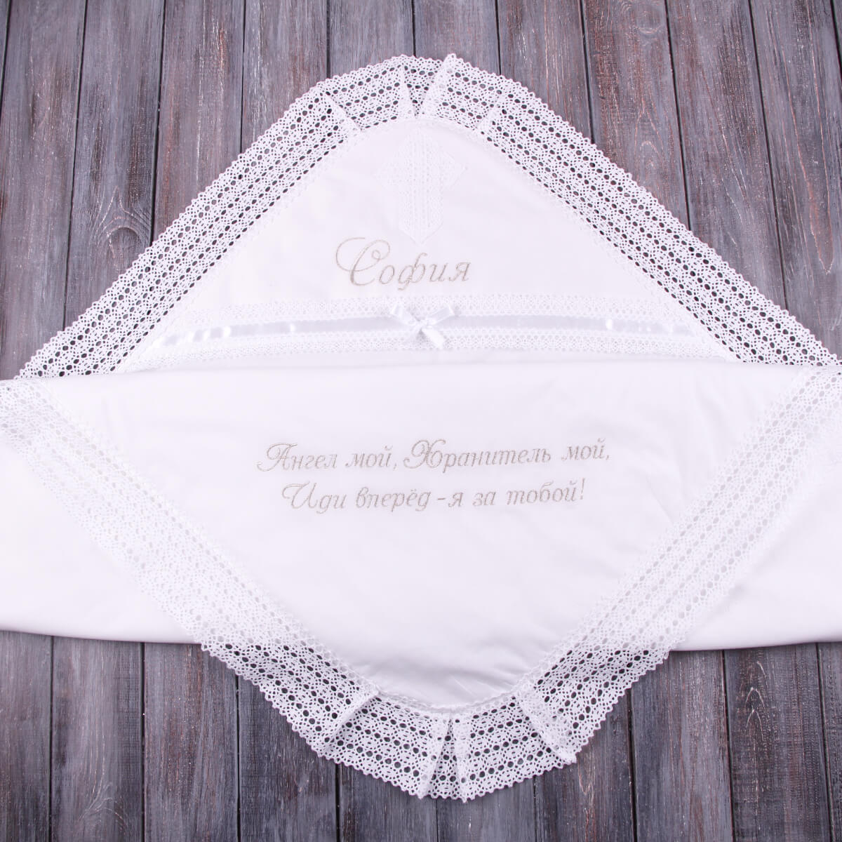 White baptism blanket. with lace trim and embroidered text on a wooden surface