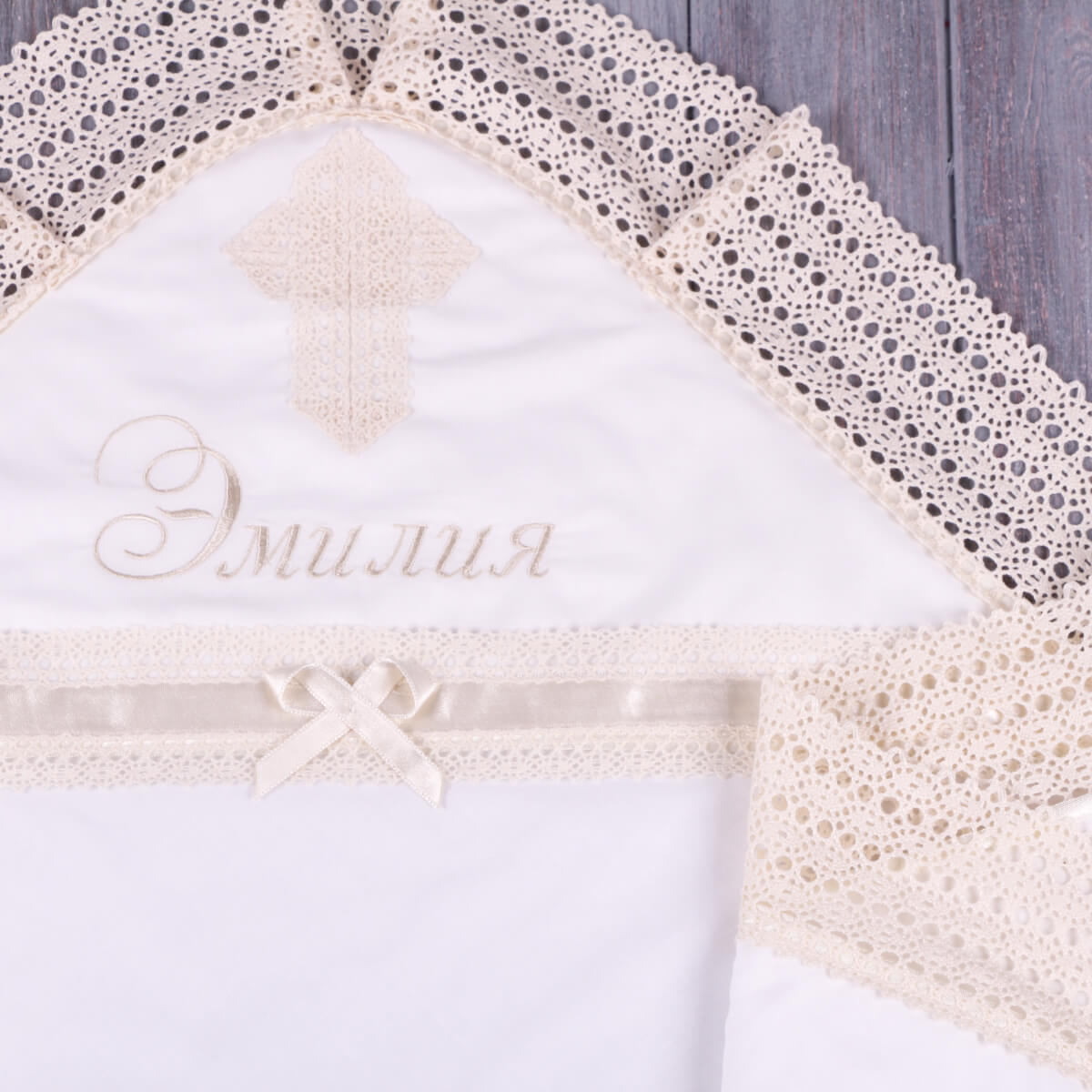 White lace-trimmed baptism blanket.with embroidered name on a wooden surface