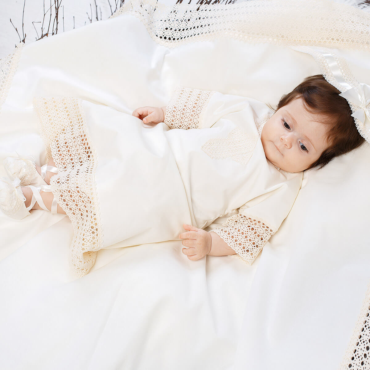 Baby wrapped in a Baptism Gown with lace details, lying on a soft surface.